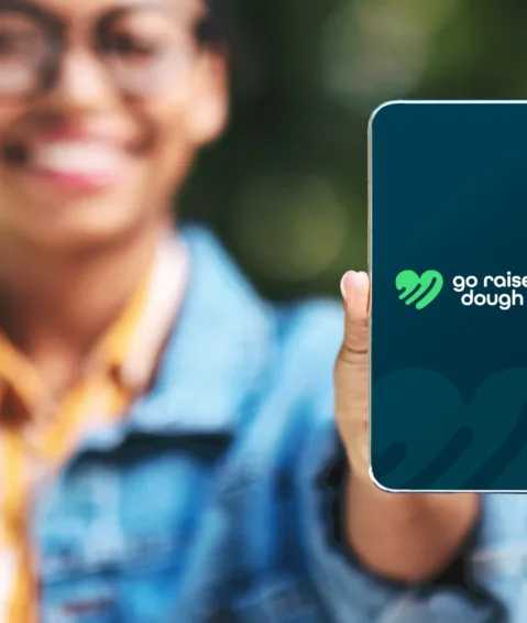 a woman holding an iPhone with go raise dough's green heart logo on a navy screen.